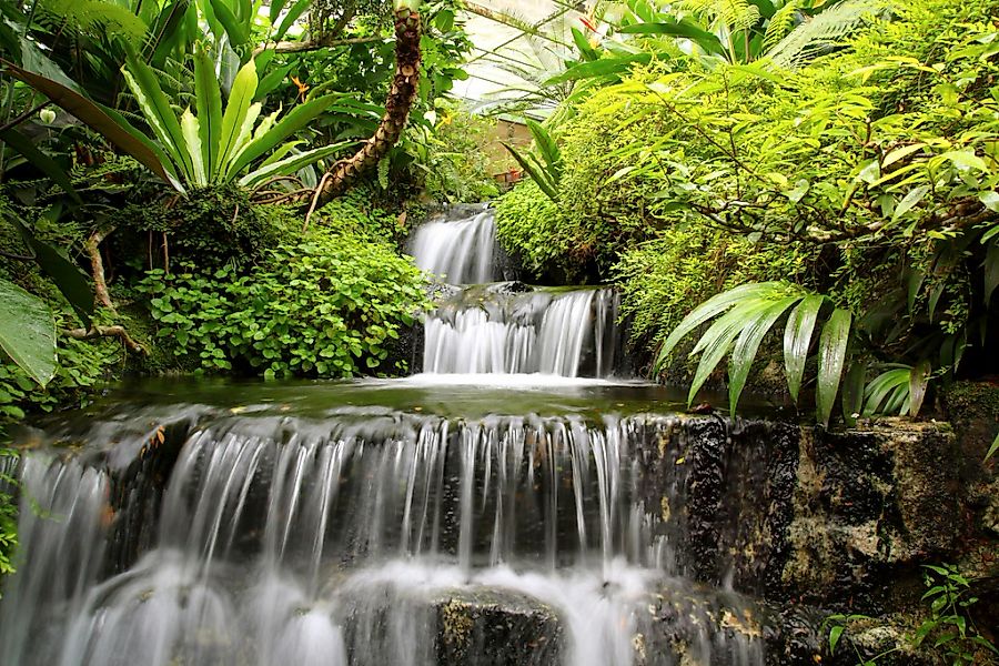 Papermoon Fototapete "WASSERFALL-BÄUME FLUSS SEE STEINE BLUMEN BERGE SONNE" günstig online kaufen